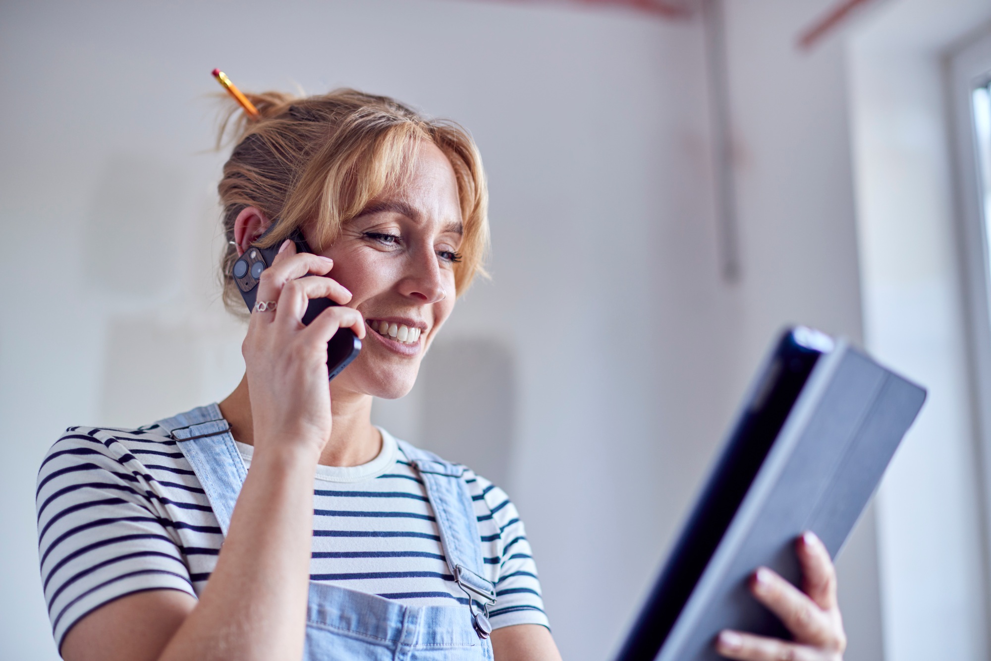 Woman Decorating Room In House Making Phone Call Looking At Digital Tablet With Paint Test Strips